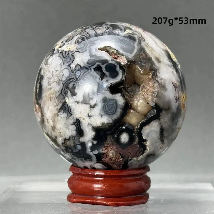 Black Cherry Blossom Agate Sphere with dramatic dark and light floral banding on a red wood stand.