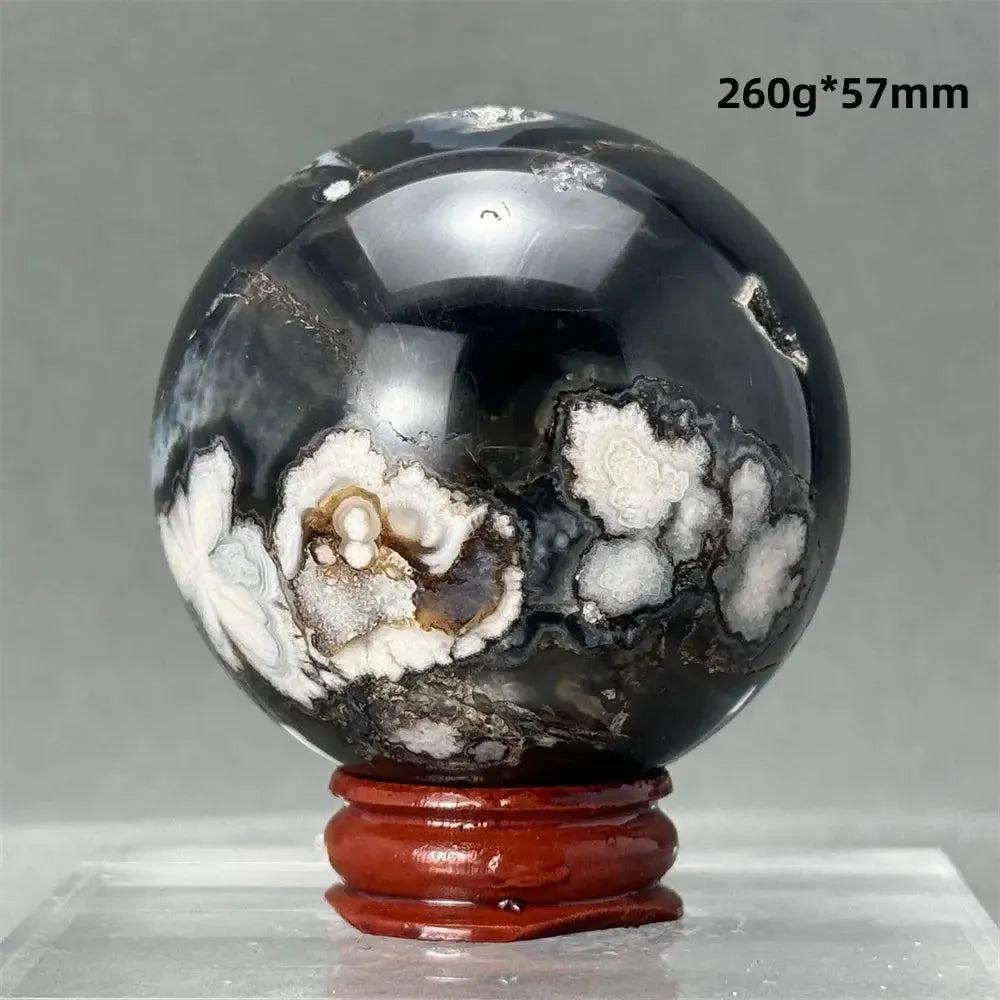 Black Cherry Blossom Agate Sphere with striking charcoal, black, creamy white, and blush pink floral patterns on a red stand.