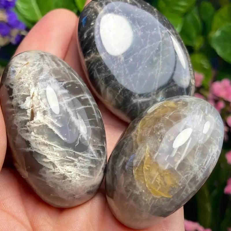 Polished black moonstone palm stones with natural veining for relaxation, held in hand for a calming crystal healing touch.
