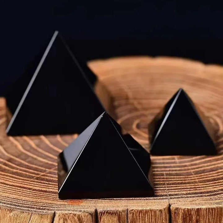 Three polished Black Obsidian Crystal Carved Protection Pyramids on a rustic wooden surface.