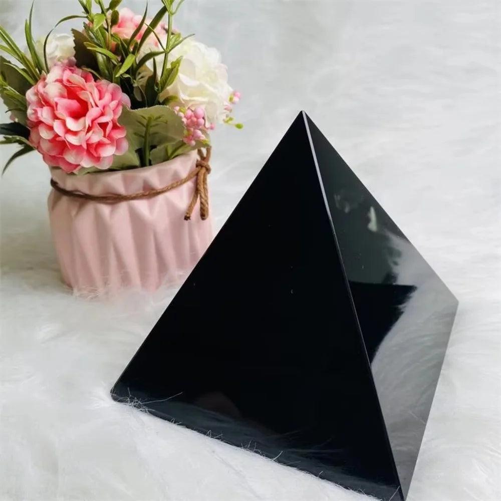 Polished black obsidian crystal pyramid for powerful protection and grounding, with a floral background.