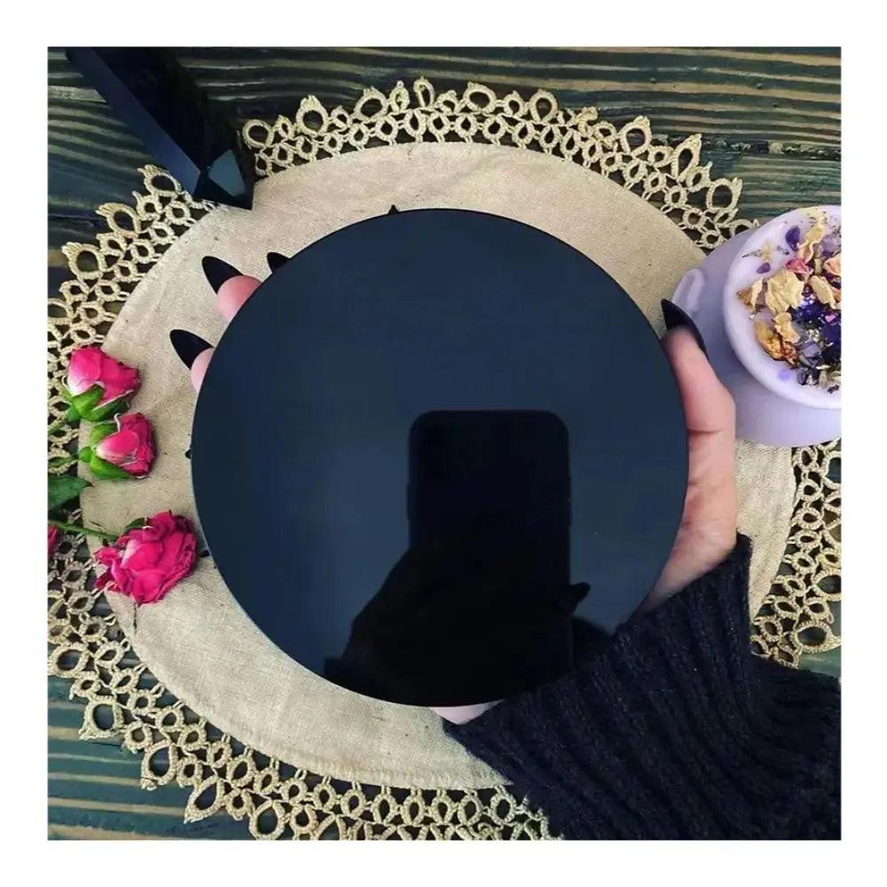 Polished black obsidian scrying mirror held by a hand, reflecting deep truth and grounding energy.