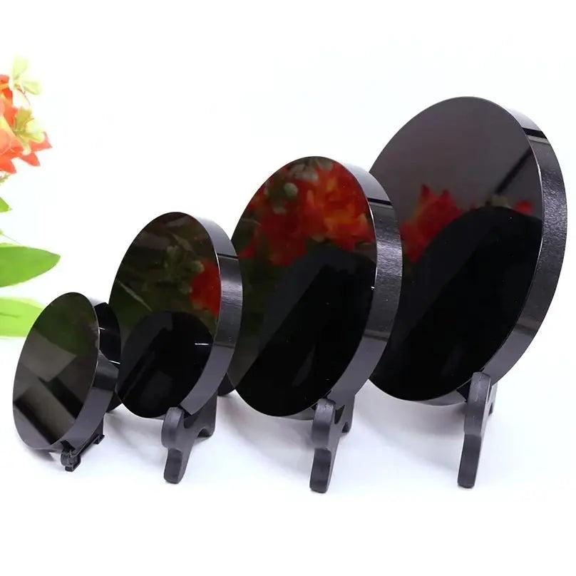 Four polished black obsidian scrying mirrors of varying sizes, each on a dark display stand.