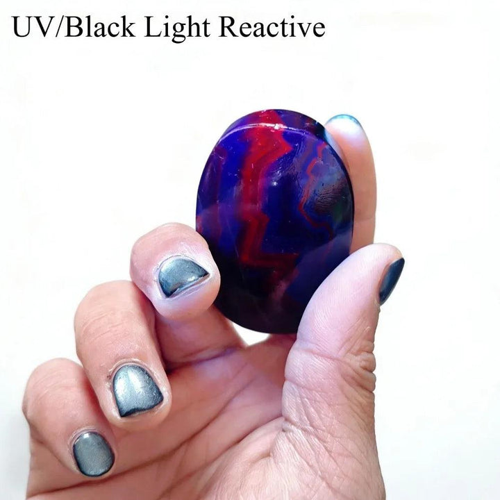 UV reactive black rose fluorite palm stone with glowing red and blue fluorescent stripes.