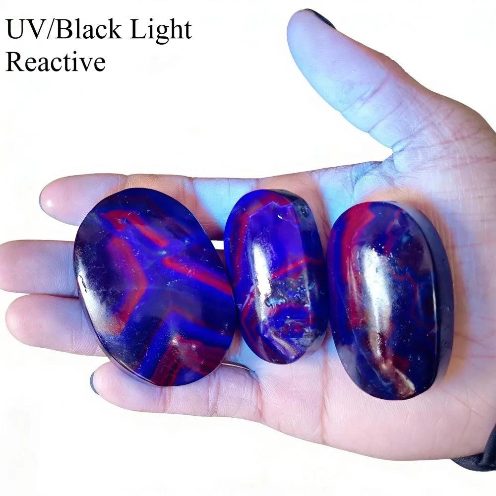 Rare Black Rose Fluorite palm stones glowing with vibrant red and blue UV-reactive stripes.