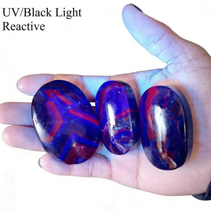 Rare Black Rose Fluorite palm stones glowing with vibrant red and blue UV-reactive stripes.