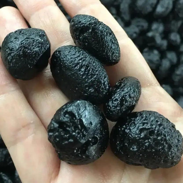 Hand holding several rough, deeply black Black Tektite Natural Meteorite Specimen Space Stones for grounding and protection.