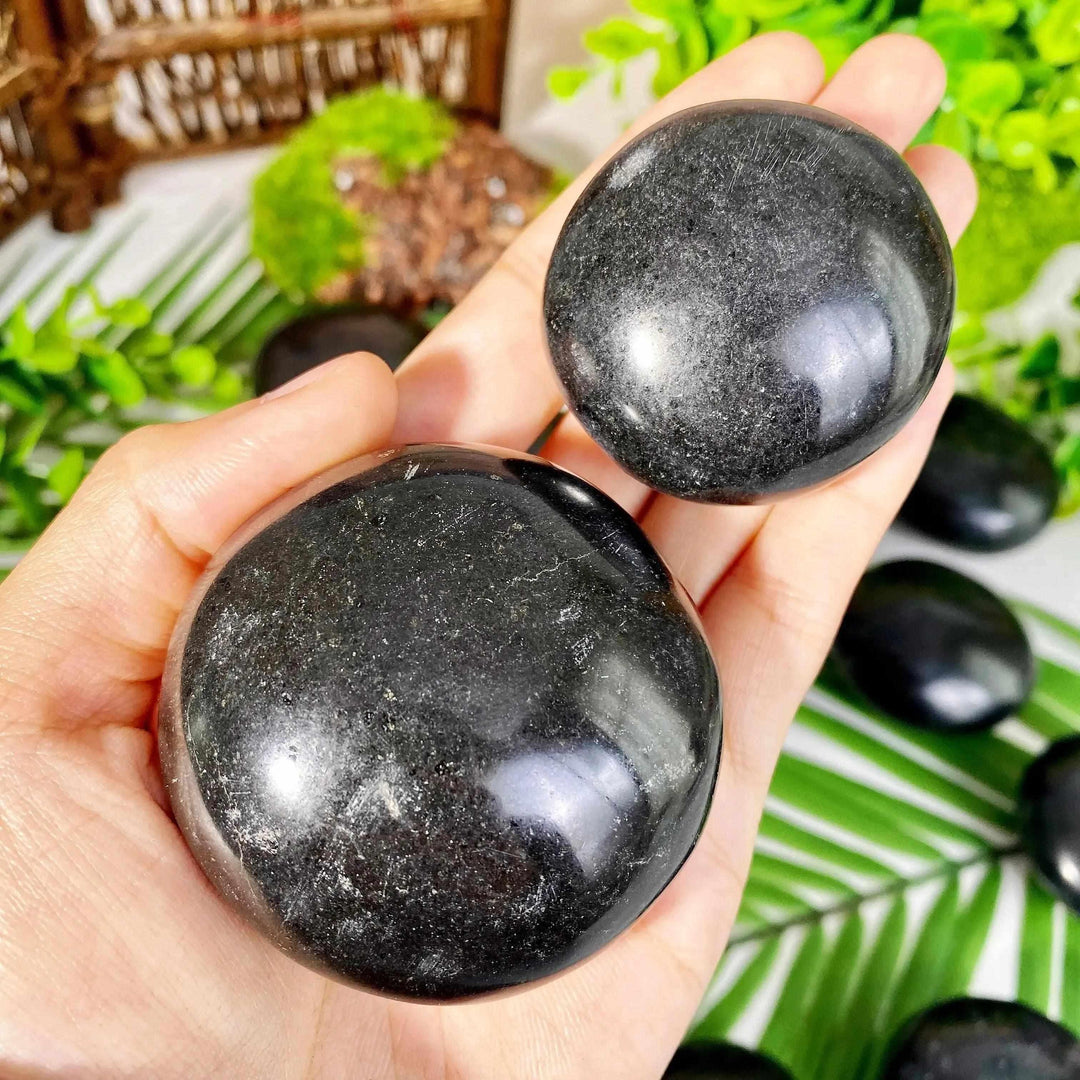 Two smooth, polished Black Tourmaline palmstones held in hand, showcasing natural striated texture for grounding.
