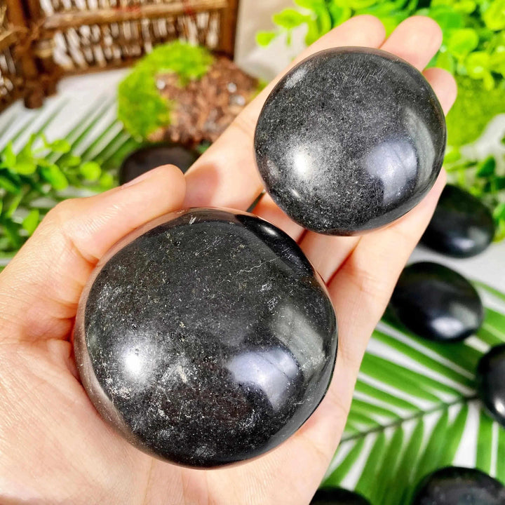 Two smooth, polished Black Tourmaline palmstones held in hand, showcasing natural striated texture for grounding.