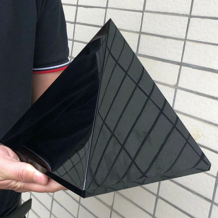 Hand holding a large, polished black tourmaline crystal pyramid, reflecting light, for protection and grounding.