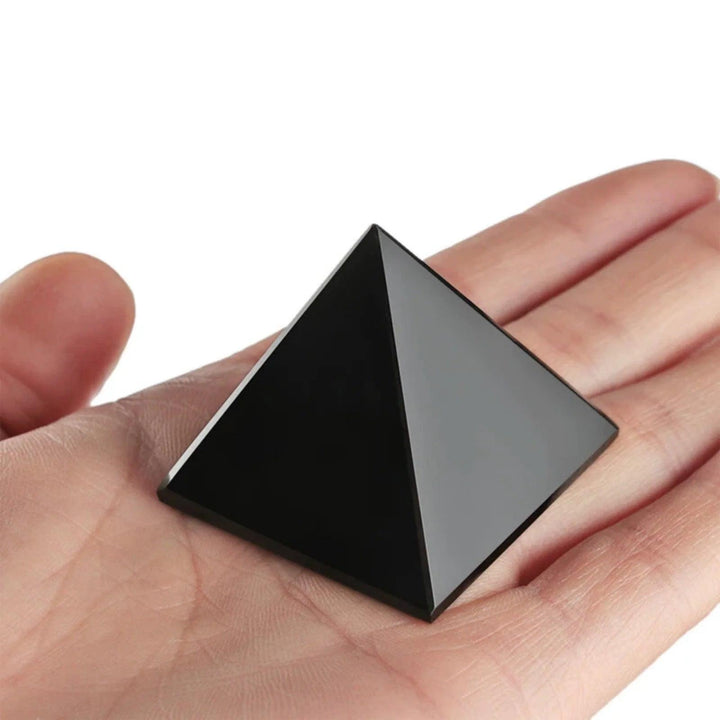 Polished black tourmaline crystal pyramid, a grounding and protective stone, held in a palm.