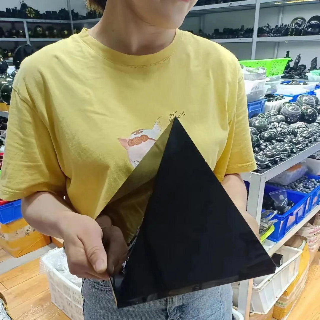 Person holding a large, polished black tourmaline crystal pyramid, showcasing its dark color and geometric shape.