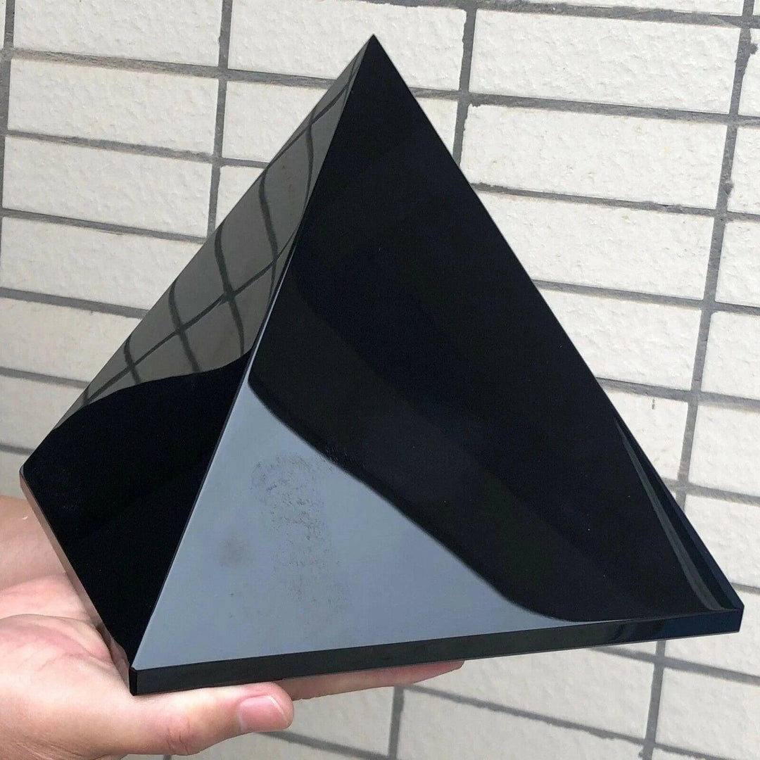 Polished black tourmaline crystal pyramid, a grounding and protective stone, held in a hand.