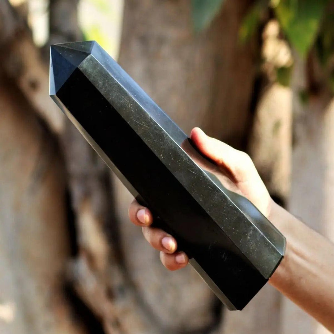 Hand holding a deeply black, raw, striated Black Tourmaline Crystal Tower for powerful protection and grounding.