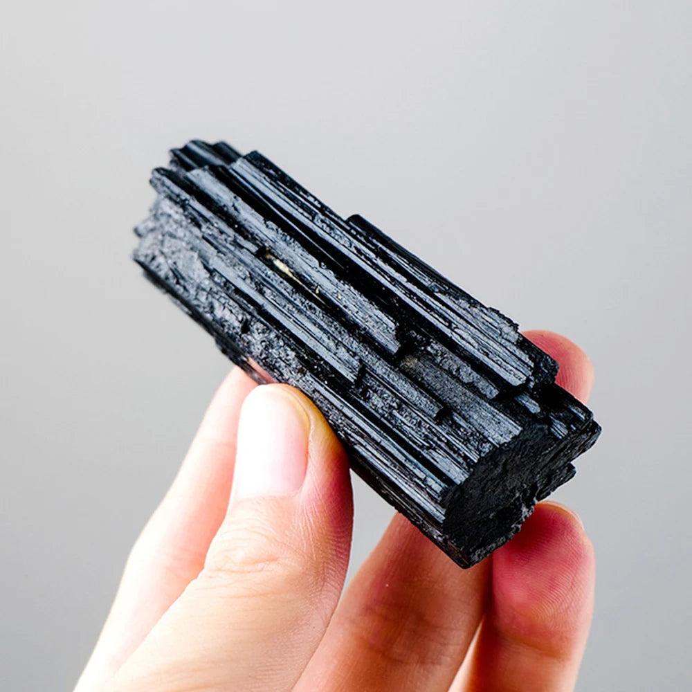 Hand holding a powerful raw Black Tourmaline crystal, showcasing its striated columnar structure for protection and grounding.