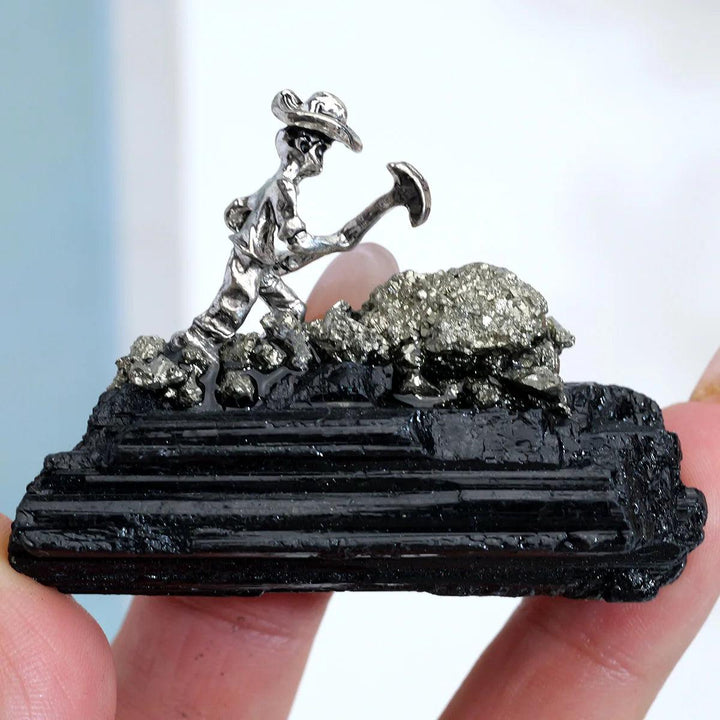 Raw Black Tourmaline specimen with a metal miner figure, featuring grounding columnar growth for Root Chakra protection.