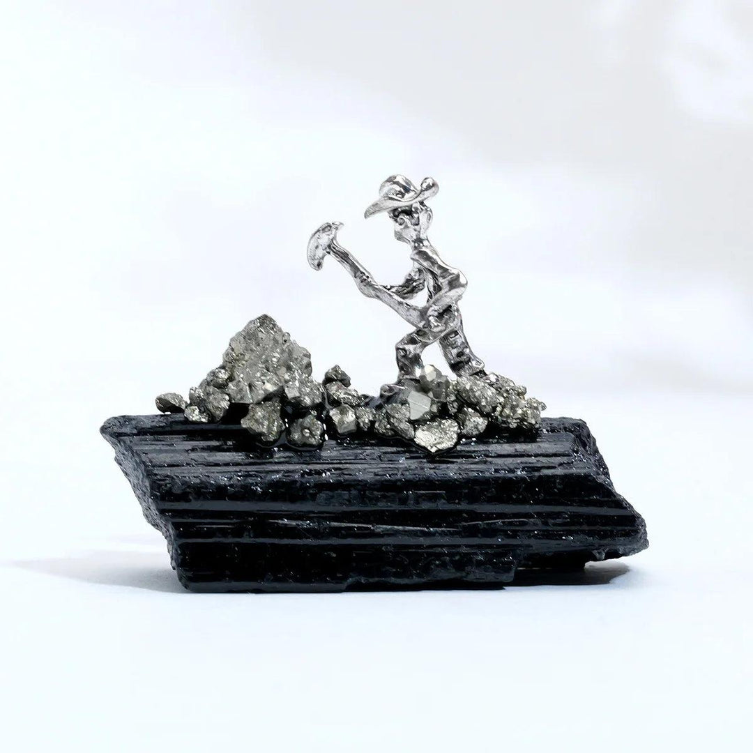 Raw black tourmaline specimen with a metal miner figure, featuring grounding columnar growth and natural striations.