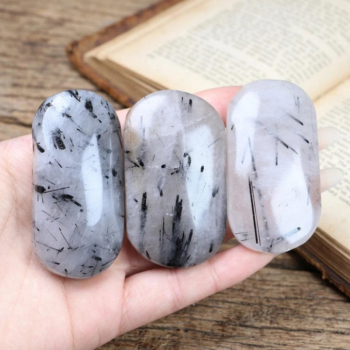 Polished tourmalinated quartz palm stones with black tourmaline needle inclusions.