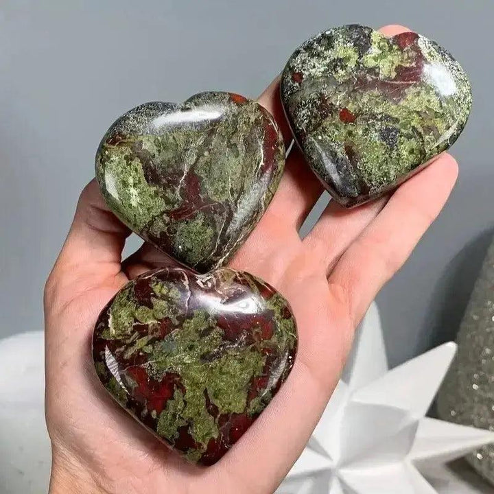 Three polished Bloodstone Heart Crystals, showcasing deep green and red flecks, held in a hand.