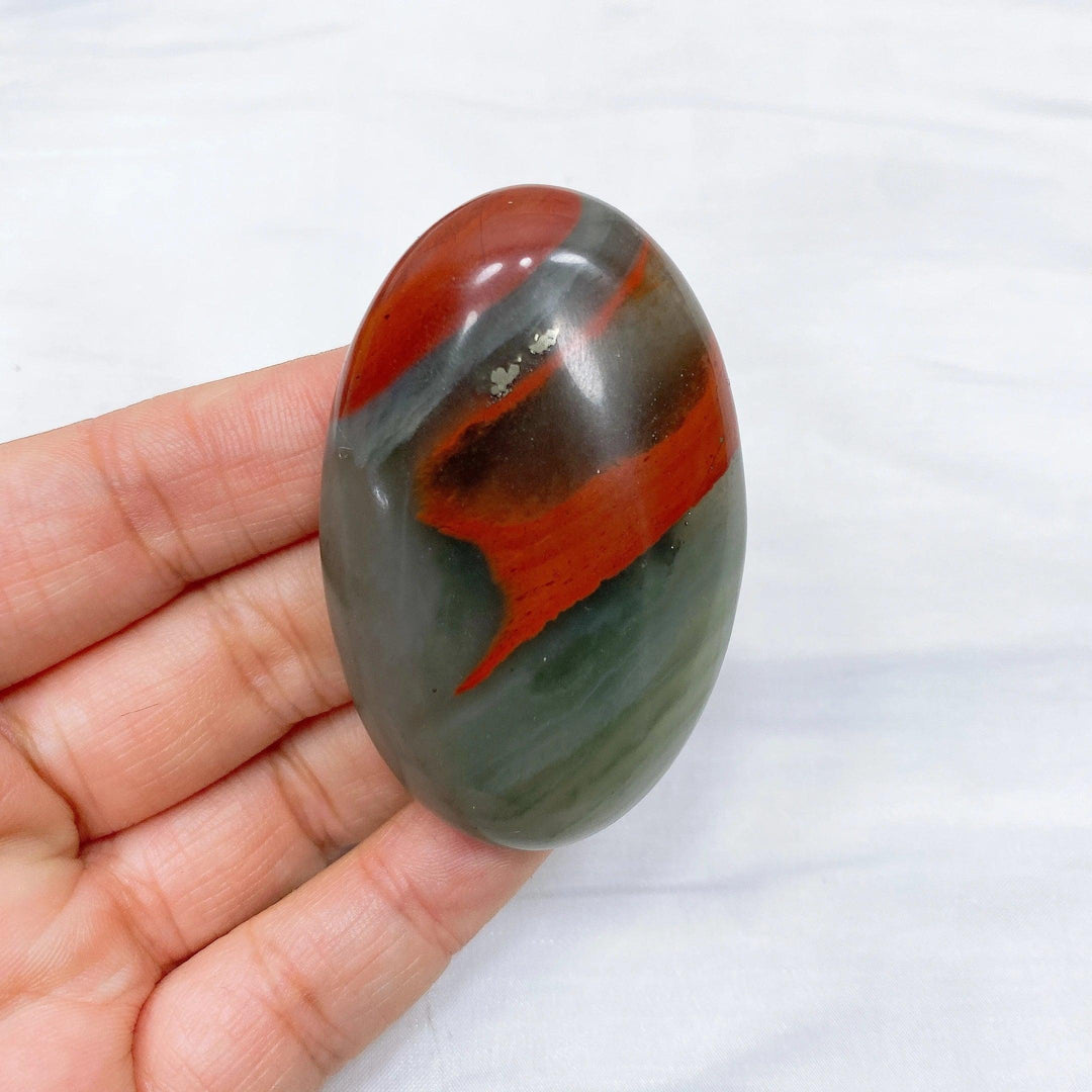 Polished Bloodstone palm stone, 50-60mm, with deep forest green and vivid red iron oxide inclusions, held in a hand.