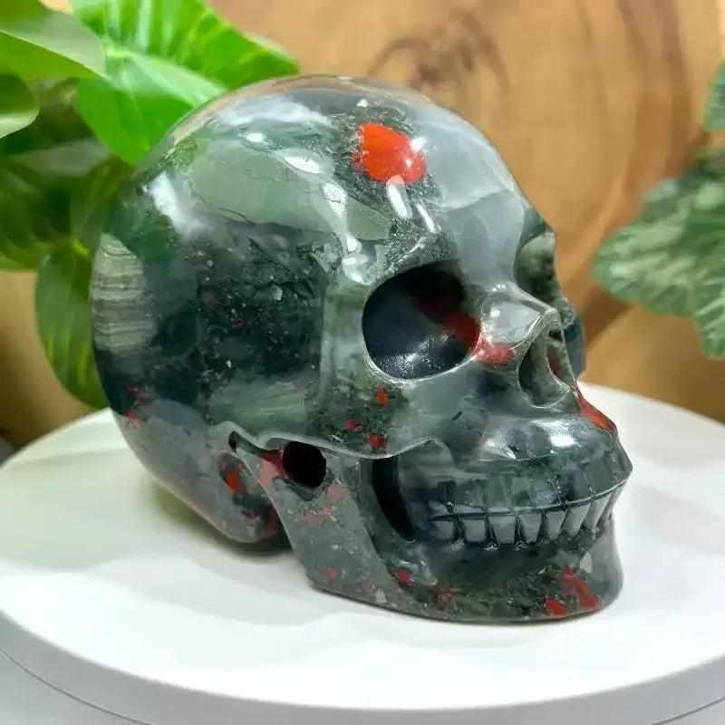Hand-polished 40-50mm Bloodstone skull carving with deep green stone and vibrant red flecks for courage and vitality.