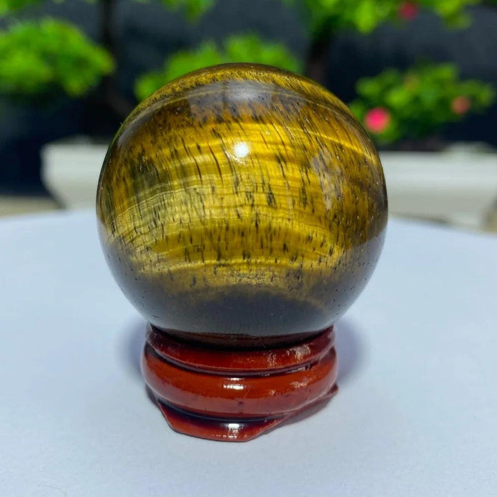 Polished natural yellow Tiger Eye crystal ball on a wooden stand, perfect for Reiki healing and spiritual home decor.