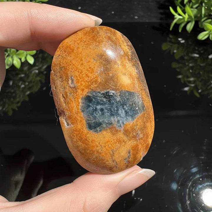 Polished orange Sunstone palm stone featuring a vibrant blue Apatite crystal center.