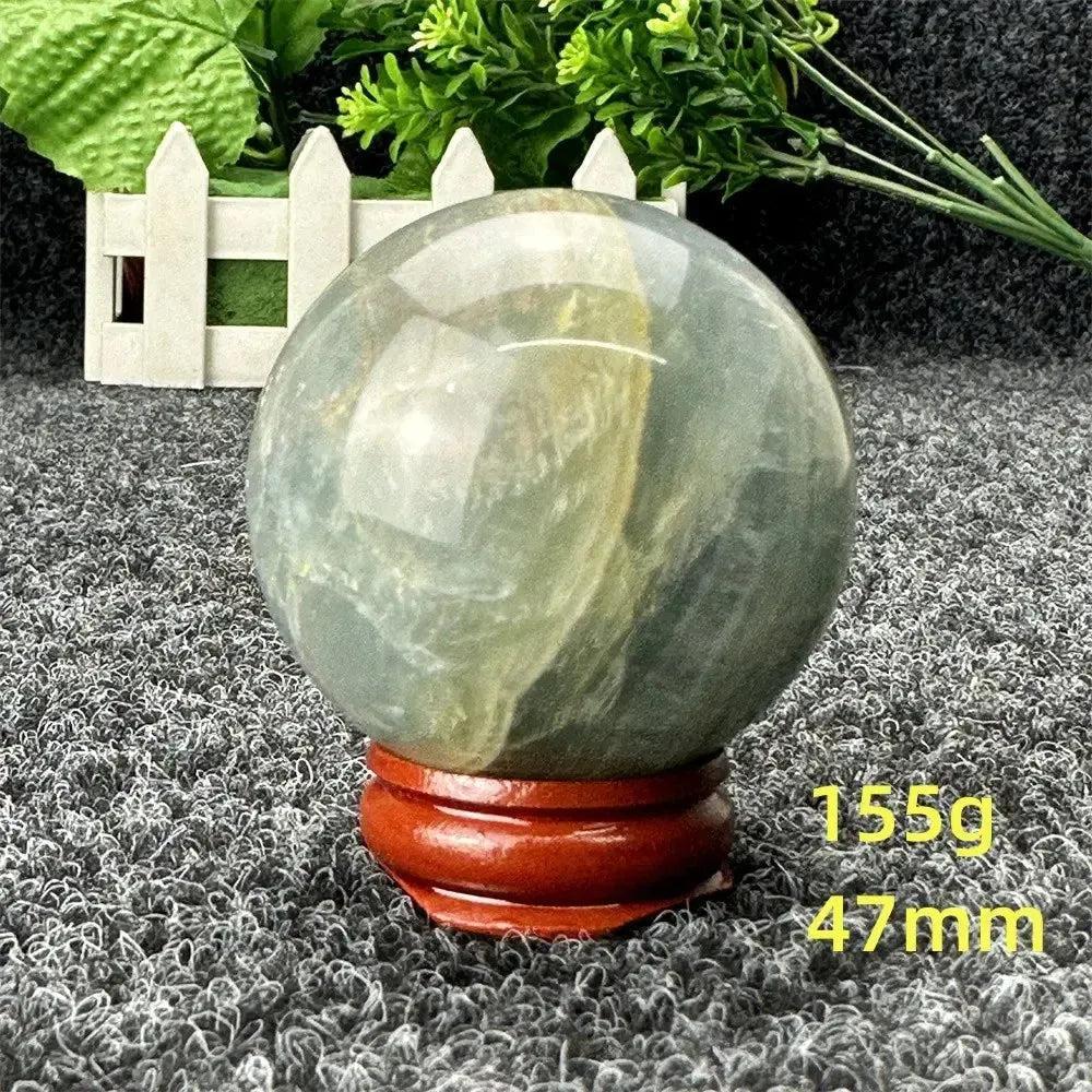 Blue Calcite Crystal Sphere: Serene, hand-polished sphere with gentle blue-green tones on a wooden stand, 47mm, 155g.