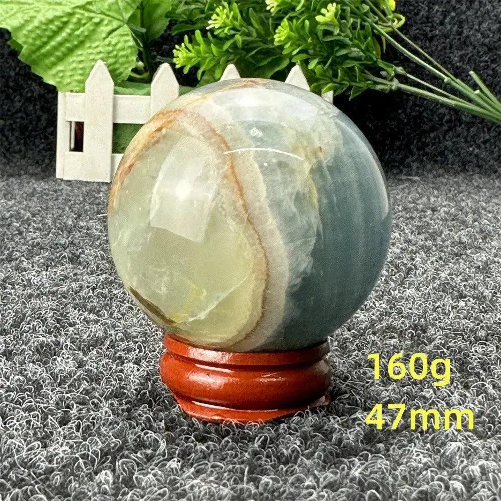 Stunning Blue Calcite Crystal Sphere, 160g, 47mm, with serene blue and green tones on a wooden stand.