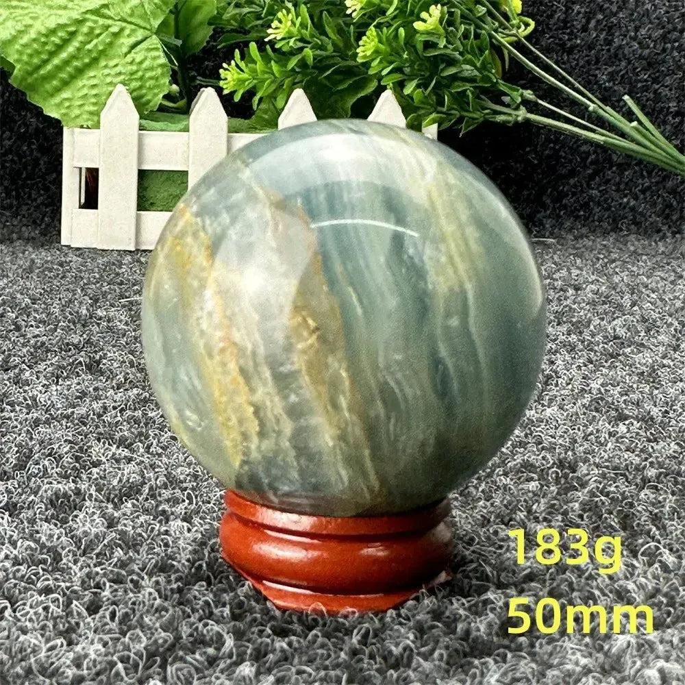 Stunning Blue Calcite Crystal Sphere, 50mm, 183g, showcasing serene blue and gold tones on a wooden stand.