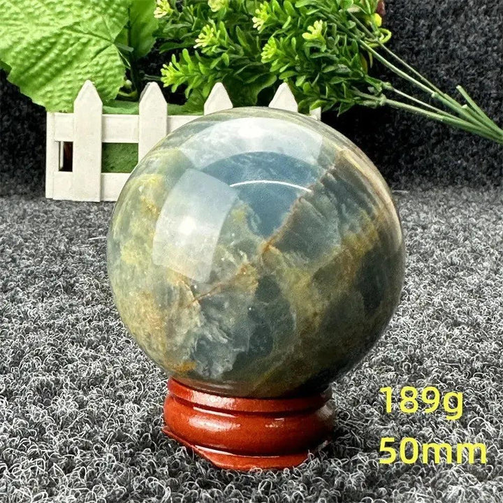 Stunning Blue Calcite Crystal Sphere, 50mm, 189g, showcasing serene blue and gold tones on a wooden stand.