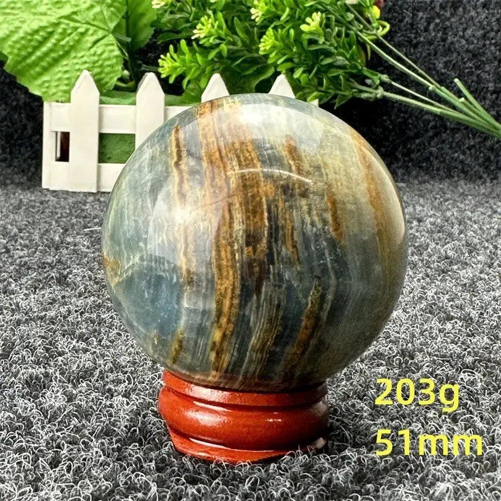 Blue Calcite Crystal Sphere: Serene blue and brown striped crystal sphere on a wooden stand, promoting peace and healing.