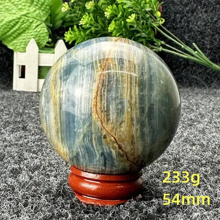 Blue Calcite Crystal Sphere: Hand-polished, serene blue and golden sphere on a wooden stand, radiating calming energy.
