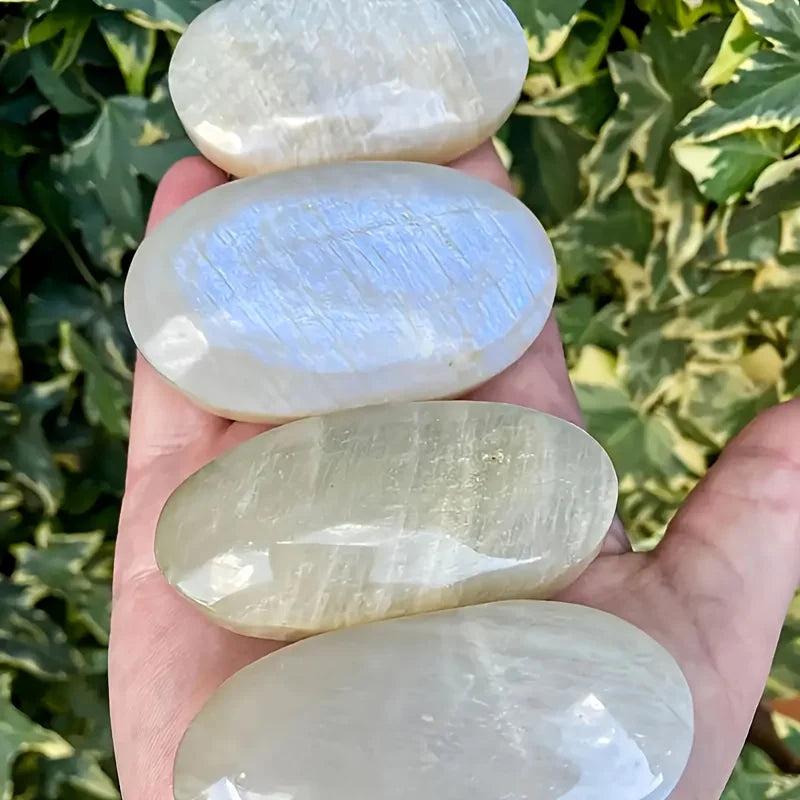 Smooth, polished Blue Moonstone oval palm stones with a shimmering blue adularescence held in a hand for meditation.