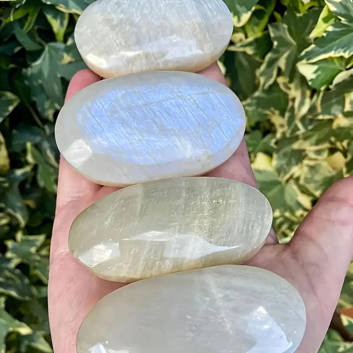 Smooth, polished Blue Moonstone oval palm stones with a shimmering blue adularescence held in a hand for meditation.