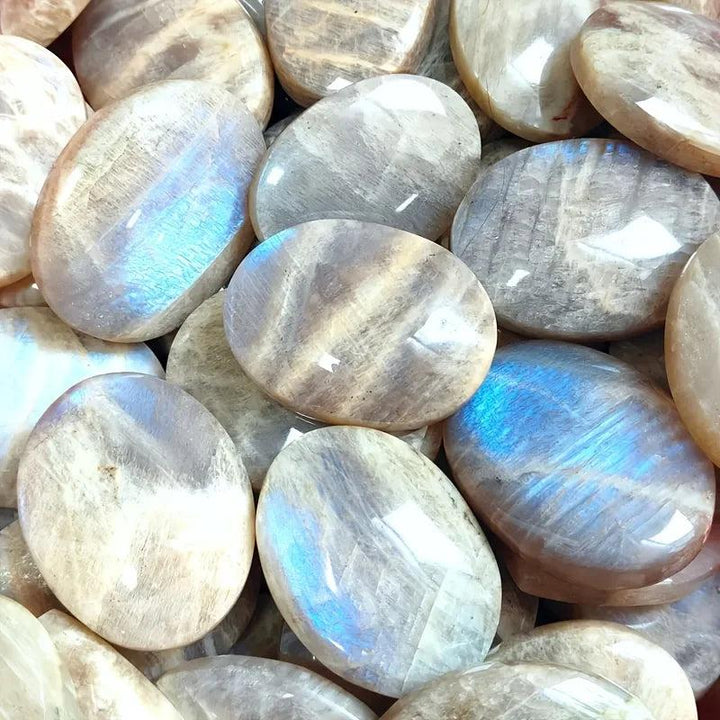 Polished blue moonstone oval palm stones featuring a shimmering blue adularescence for meditation and chakra healing.