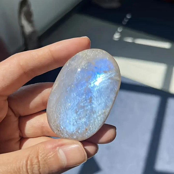 Polished blue moonstone oval palm stone featuring a shimmering blue adularescence for meditation and chakra healing.