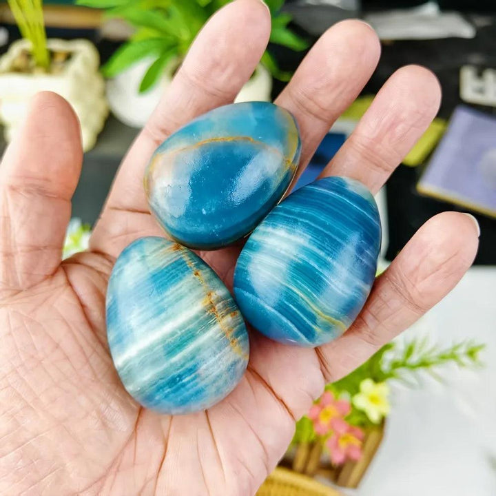 Three polished Blue Onyx crystal eggs, with cool layered blue and white banding, held in a hand for calm and clarity.