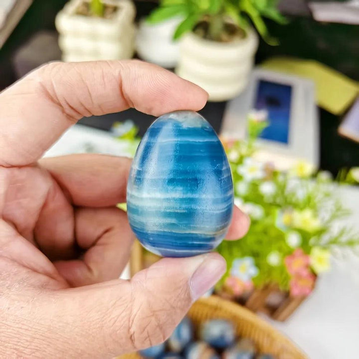 Hand holding a polished Blue Onyx Crystal Egg, showcasing its cool, layered blue hues and natural banding for calm and clarity.