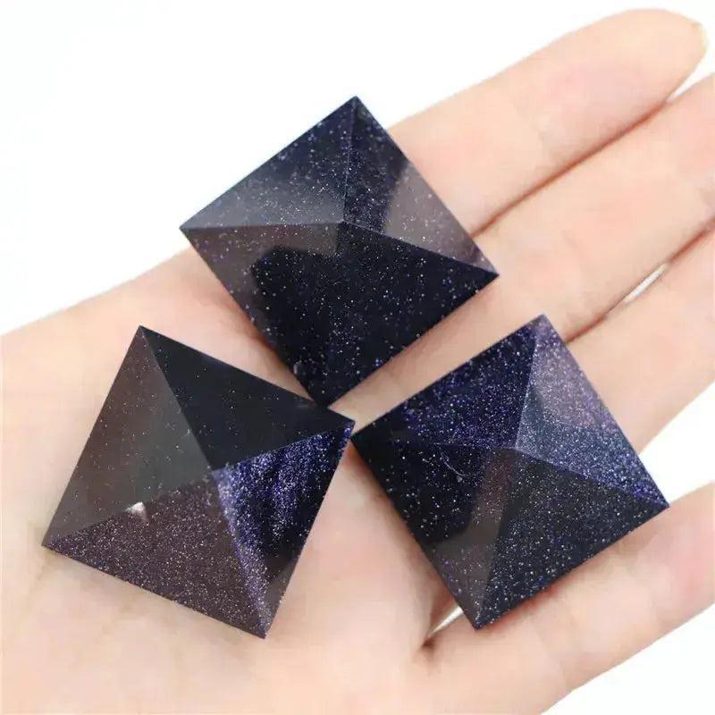 Three shimmering deep blue sandstone crystal pyramids with golden flecks, held in a hand by Crystal Destiny.