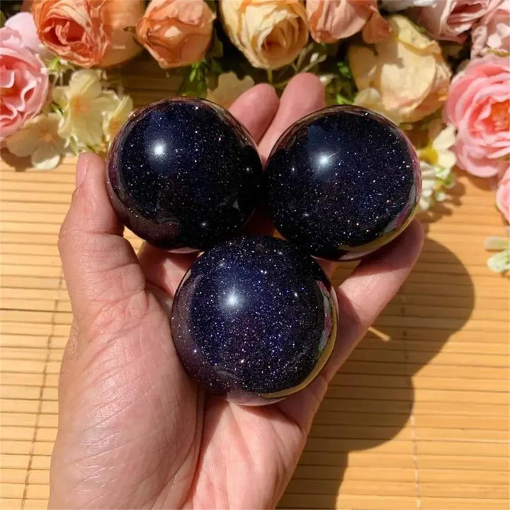 Three shimmering blue sandstone spheres in a hand, evoking a starlit night sky, from Crystal Destiny.