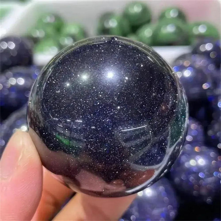 Crystal Destiny's polished Blue Sandstone sphere, deep blue with shimmering golden sparkles, inspiring ambition.