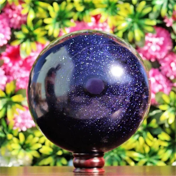 Polished Blue Sandstone sphere from Crystal Destiny, shimmering with golden sparkles on a dark blue base.