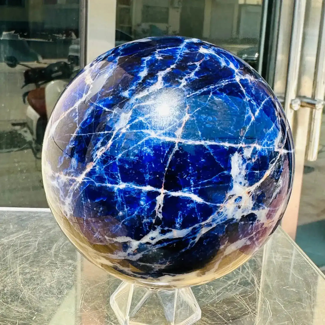 Polished Blue Sodalite sphere featuring deep blue tones and striking white veins for Throat Chakra healing and display.