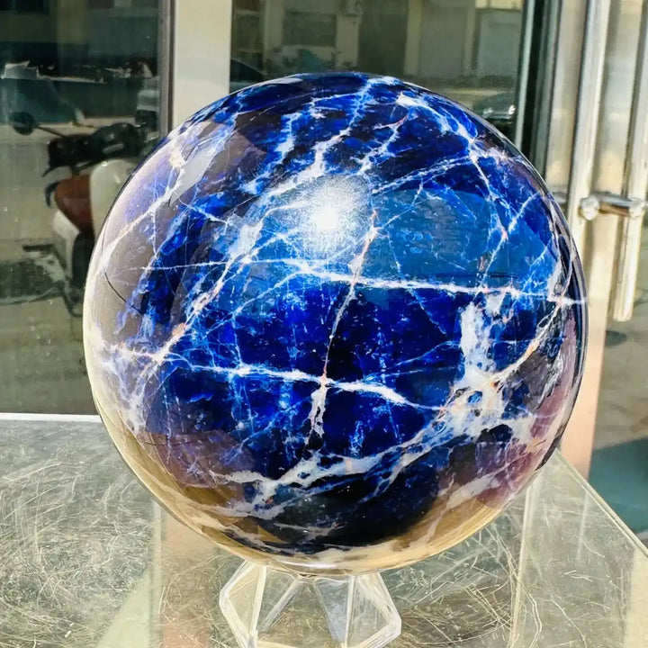 Polished Blue Sodalite sphere featuring deep blue tones and striking white veins for Throat Chakra healing and display.