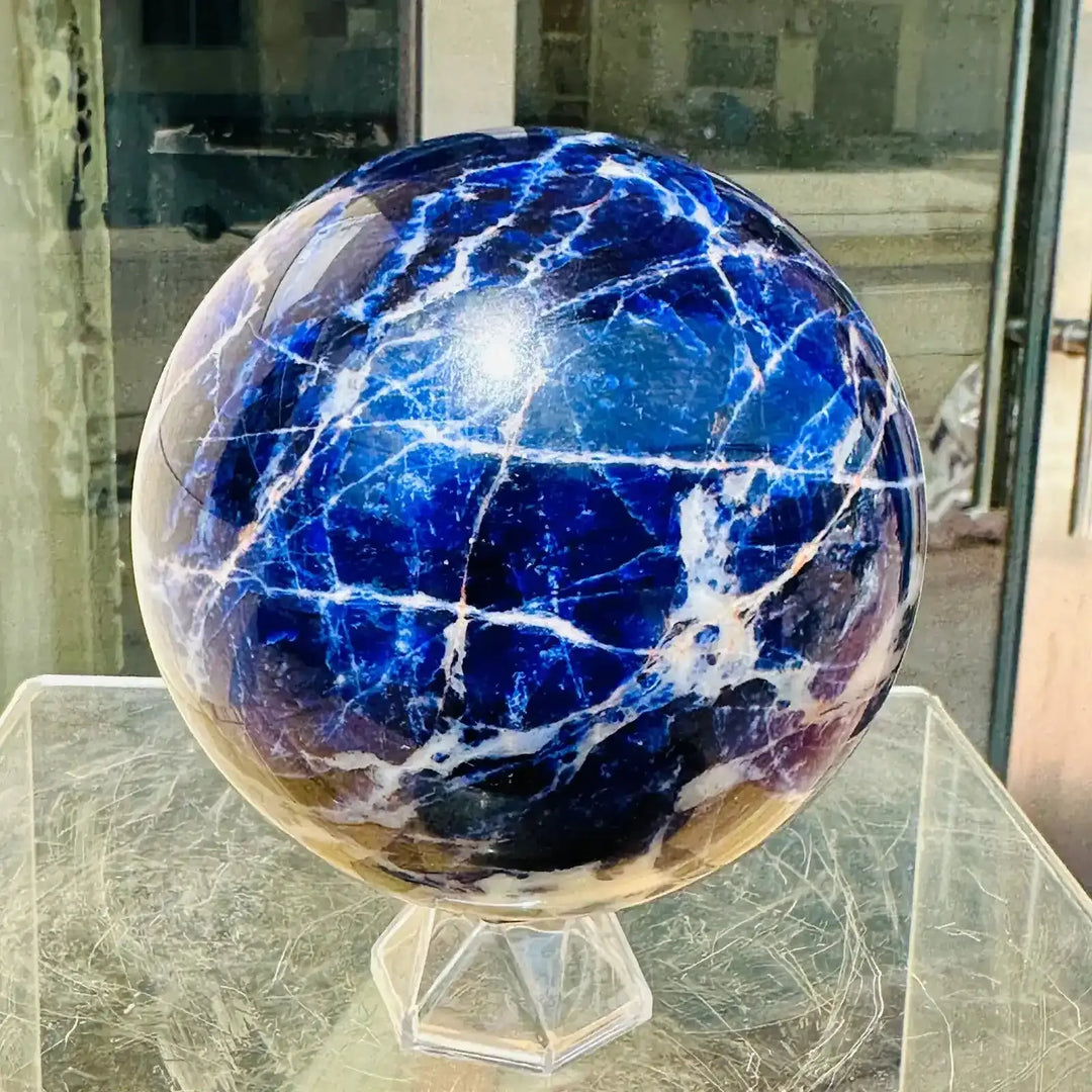 Polished blue sodalite sphere with striking white veins, perfect for Throat Chakra healing and home display.