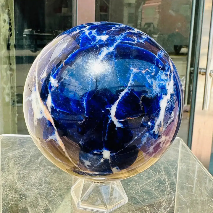 Polished Blue Sodalite sphere featuring deep blue tones and striking white veins for Throat and Third Eye Chakra healing.