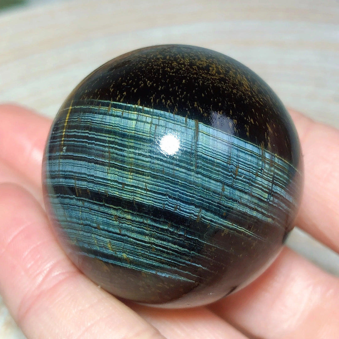 Flashy blue and yellow Tiger Eye crystal sphere, a polished natural stone ball for healing, energy, and home decor.