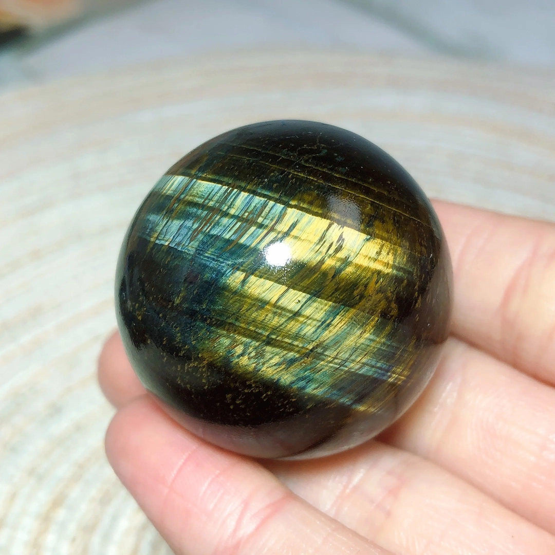 Flashy blue and yellow Tiger Eye crystal sphere, a polished natural stone ball for healing energy and home decor.