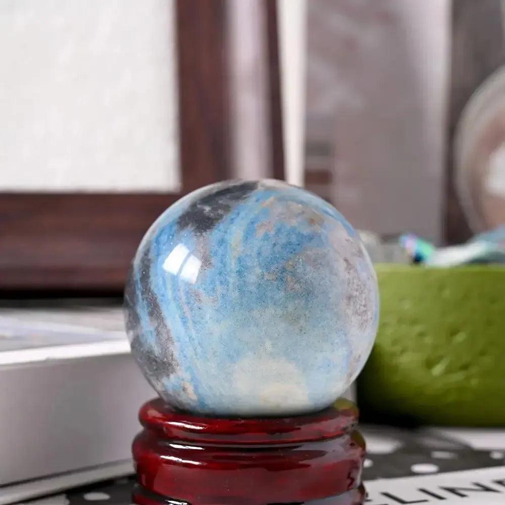 Polished Blue Trolleite sphere on a wooden stand from Crystal Destiny, showcasing blue-gray hues for spiritual insight.